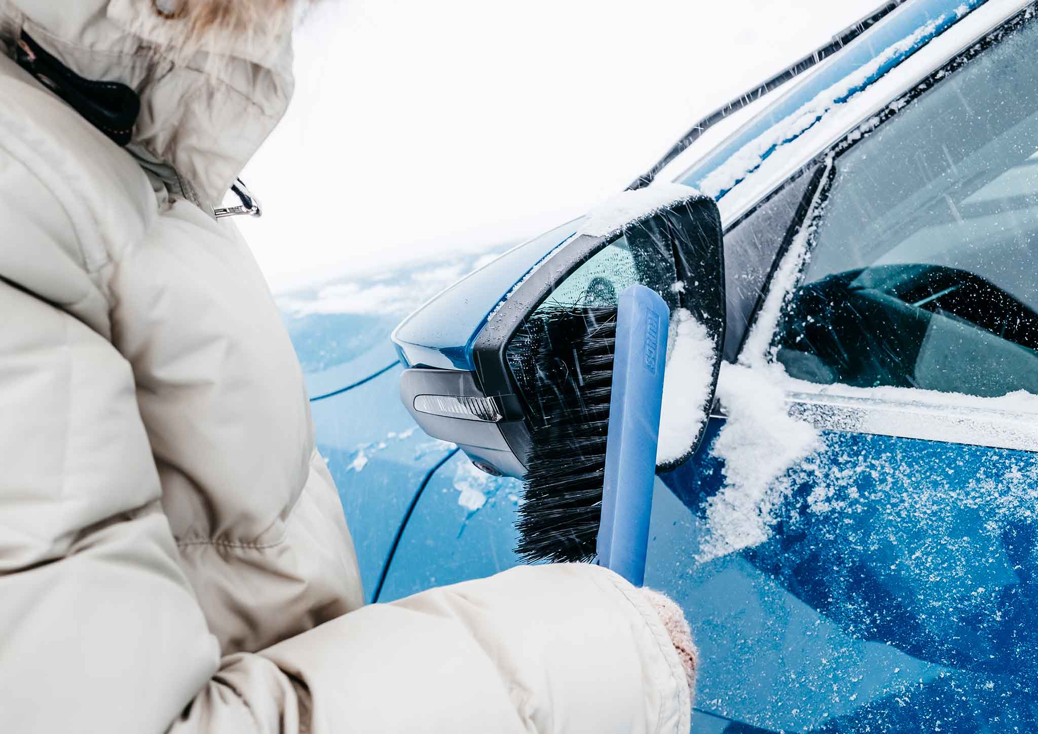 Person kehrt vom Dach eines Autos mit einem Besen den Schnee ab